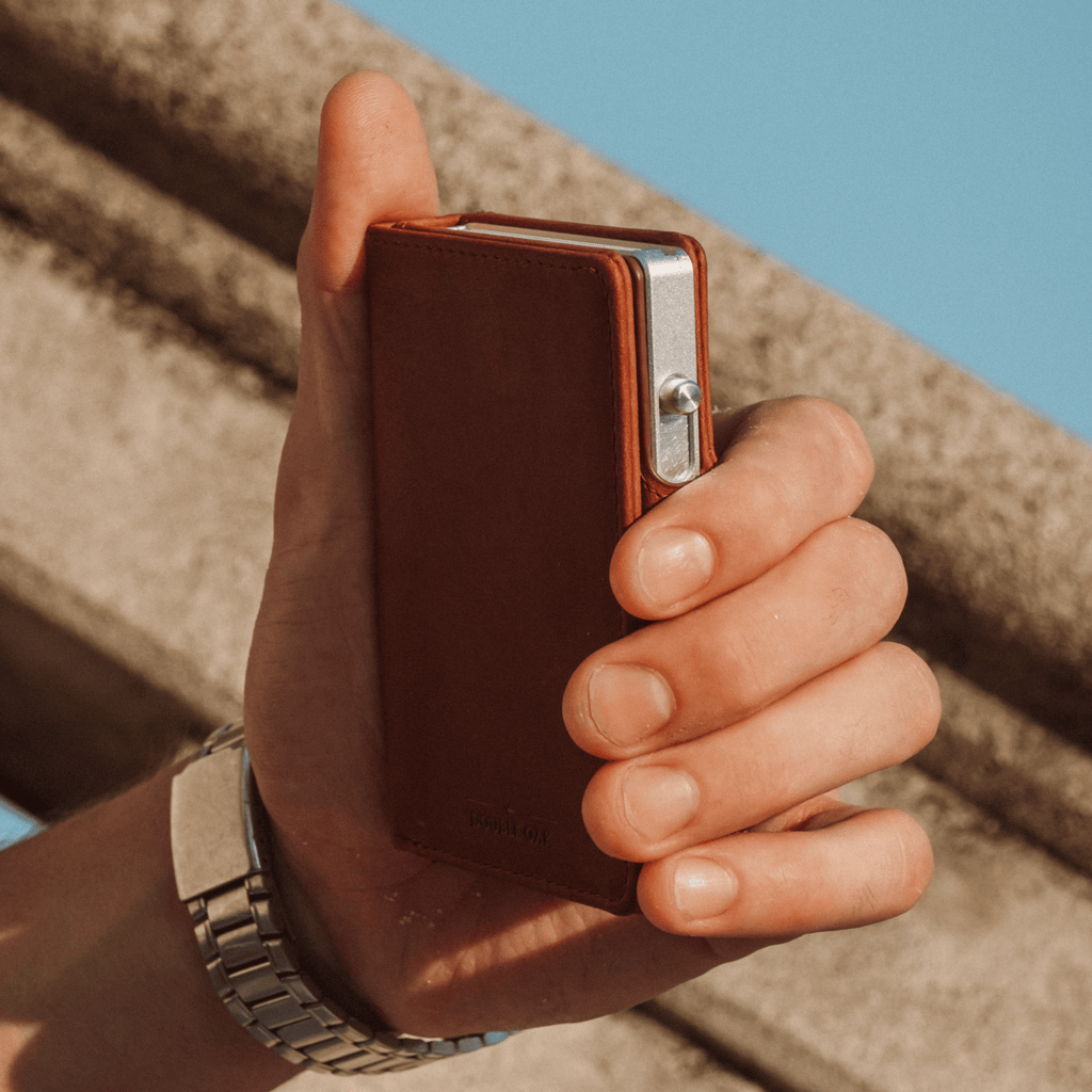 Brown leather bifold wallet held in hand with snap clasp and card compartment