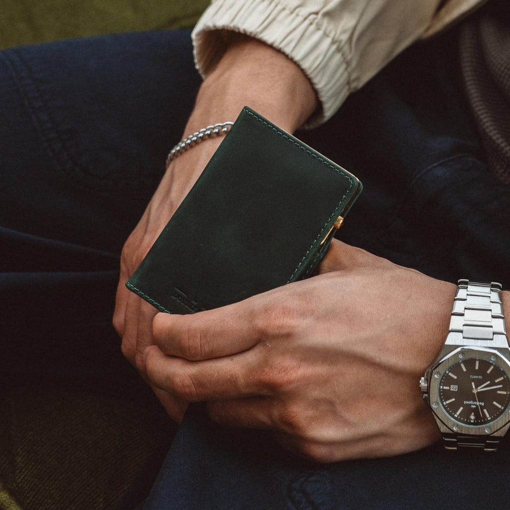 Green bifold wallet in hand with visible front panel stitching and metal edge