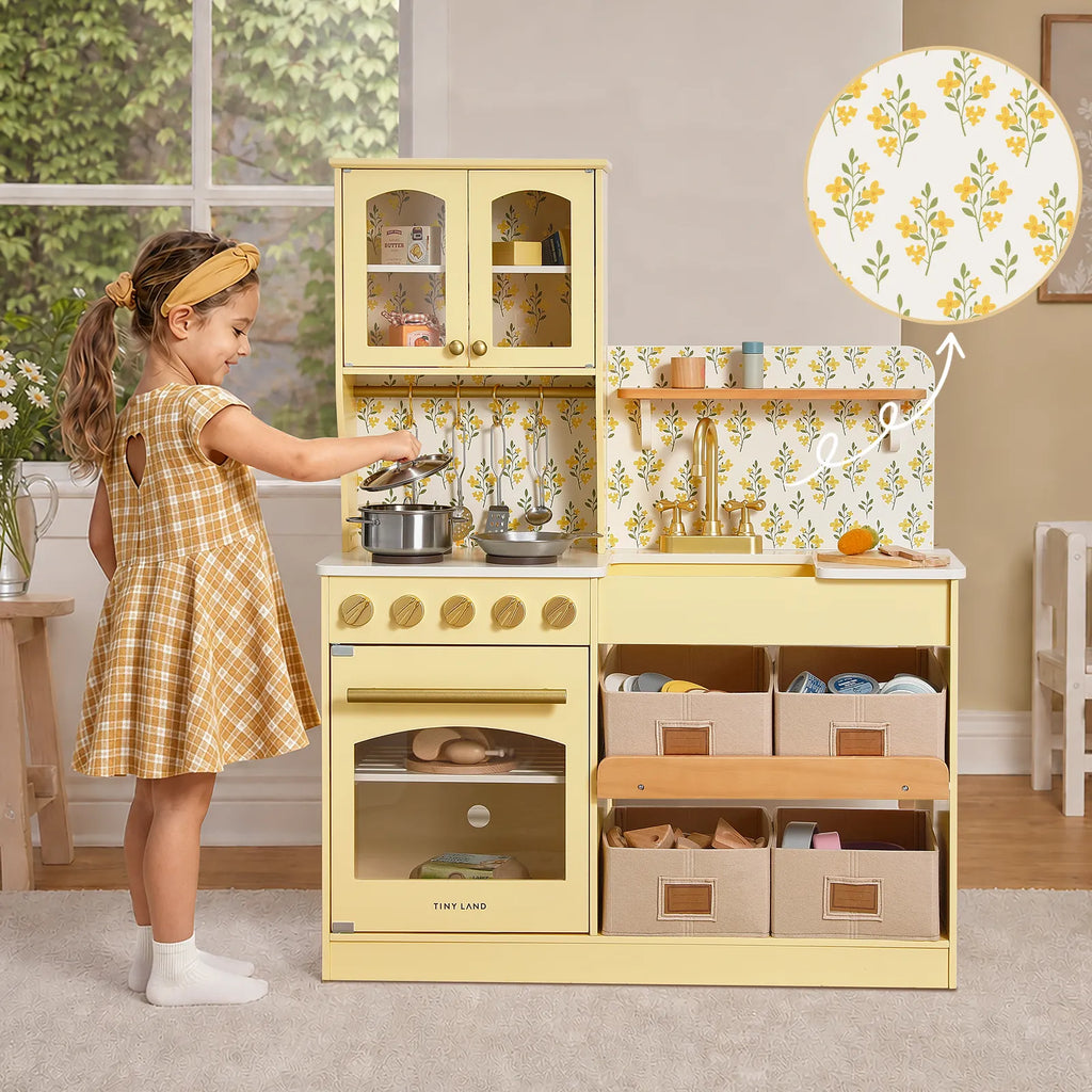 Yellow wooden play kitchen with child reaching toward the stove and sink