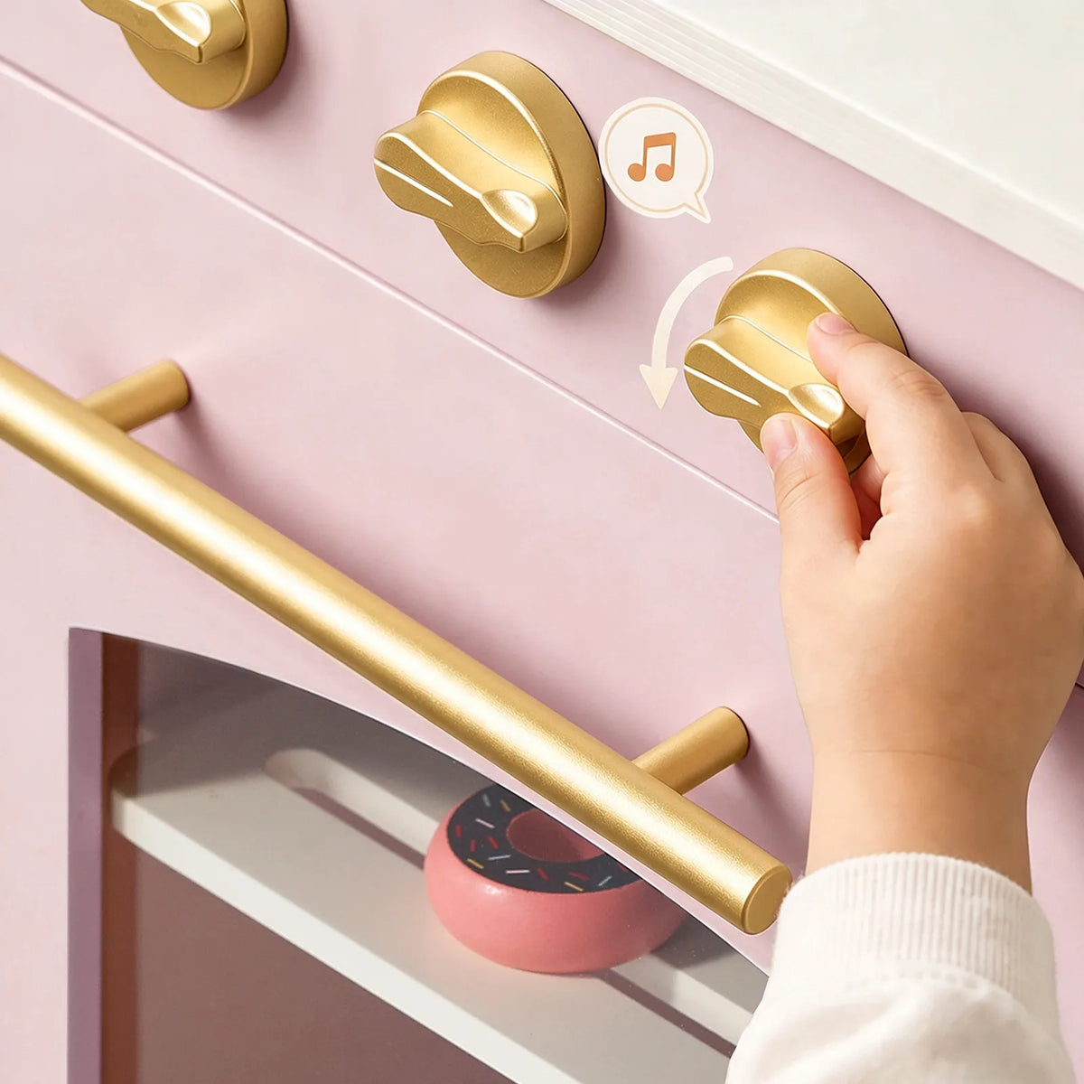 Gold-tone cabinet handles on a light pink wooden play kitchen