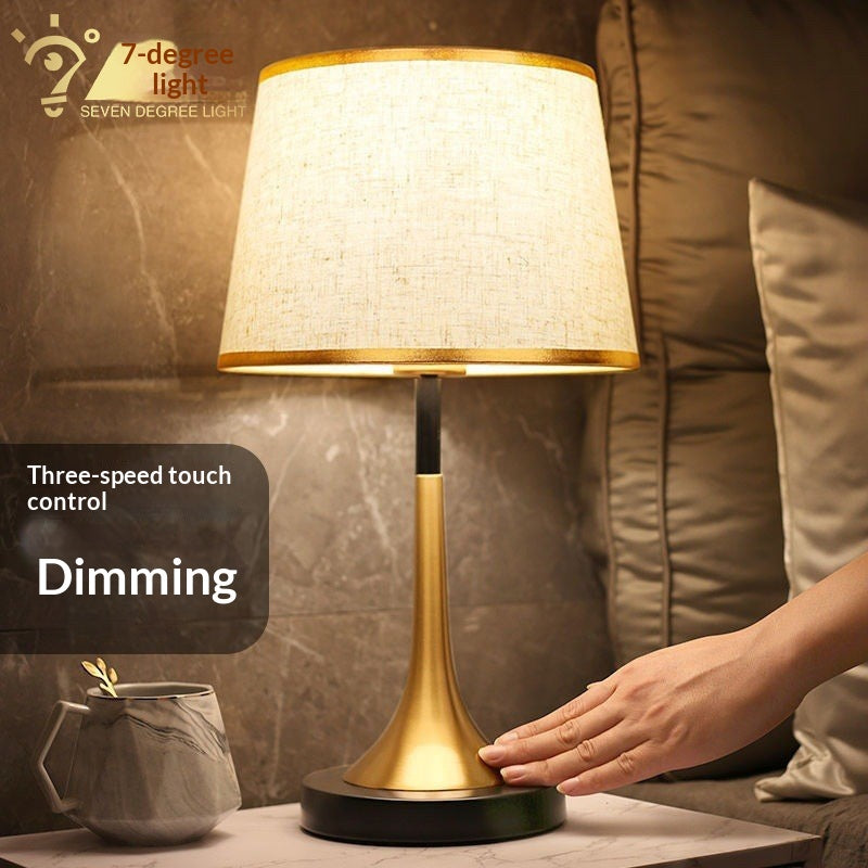 Gold table lamp with off-white fabric shade and dark round base, touch control-ready