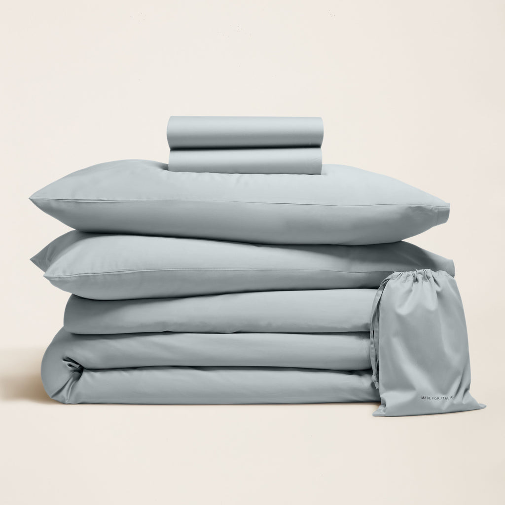 Light gray sateen bedding bundle with stacked sheets, pillowcases, and drawstring bag