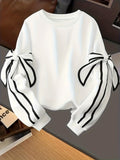 White crewneck long-sleeve sweater with black striped ribbon bow sleeves, folded view.