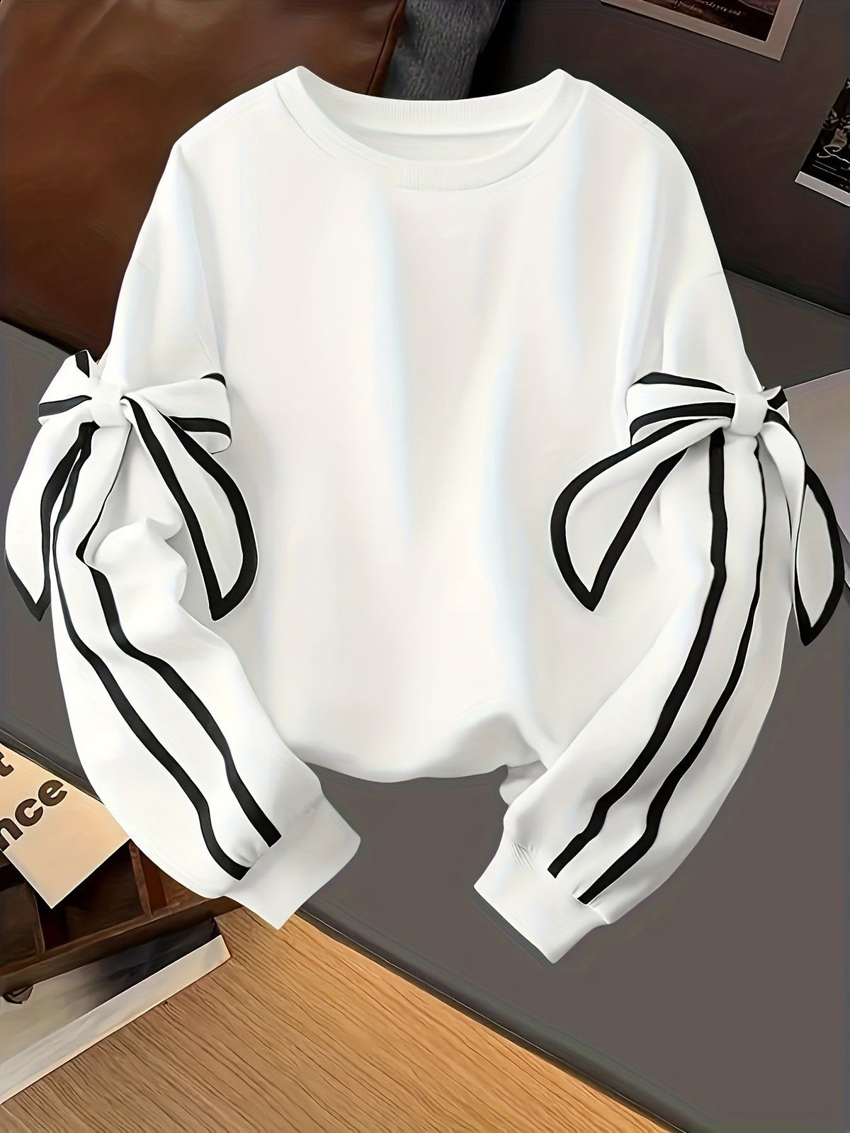 White crewneck long-sleeve sweater with black striped ribbon bow sleeves, folded view.