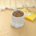 White ceramic cat bowl with paw-foot shape, filled with dry kibble
