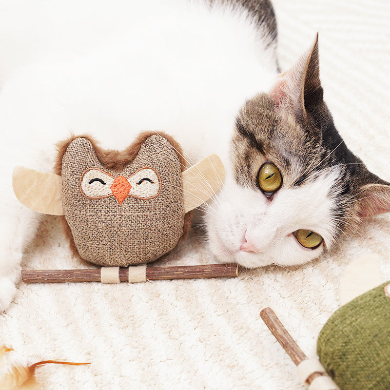 Catnip owl teething stick with green plush owl on wooden perch, cat nearby