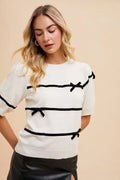 White knit top with black horizontal stripes and bow accents at neckline and sleeves