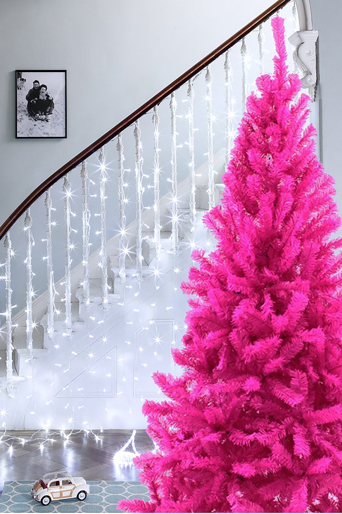 Pink artificial Christmas tree with dense branches on a white stand base