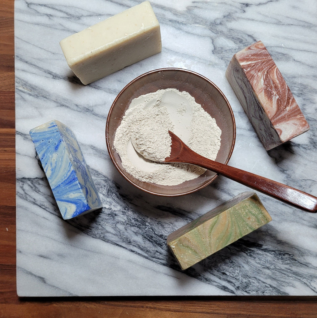 Assorted cold-processed soap bars on marble: white, blue, brown, and green.