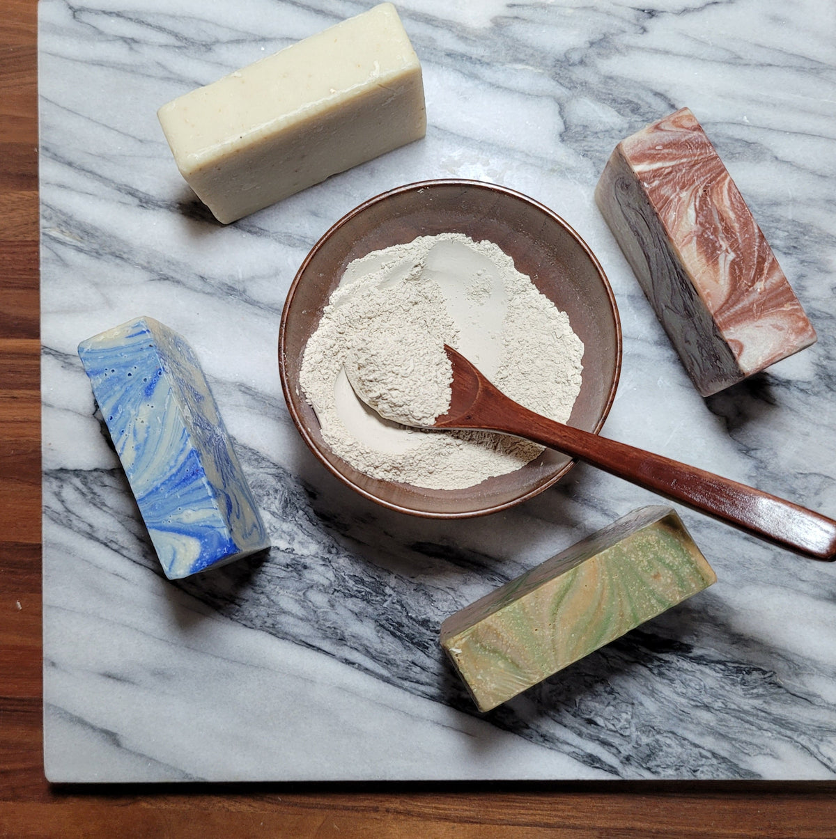 Assorted cold-processed soap bars on marble: white, blue, brown, and green.