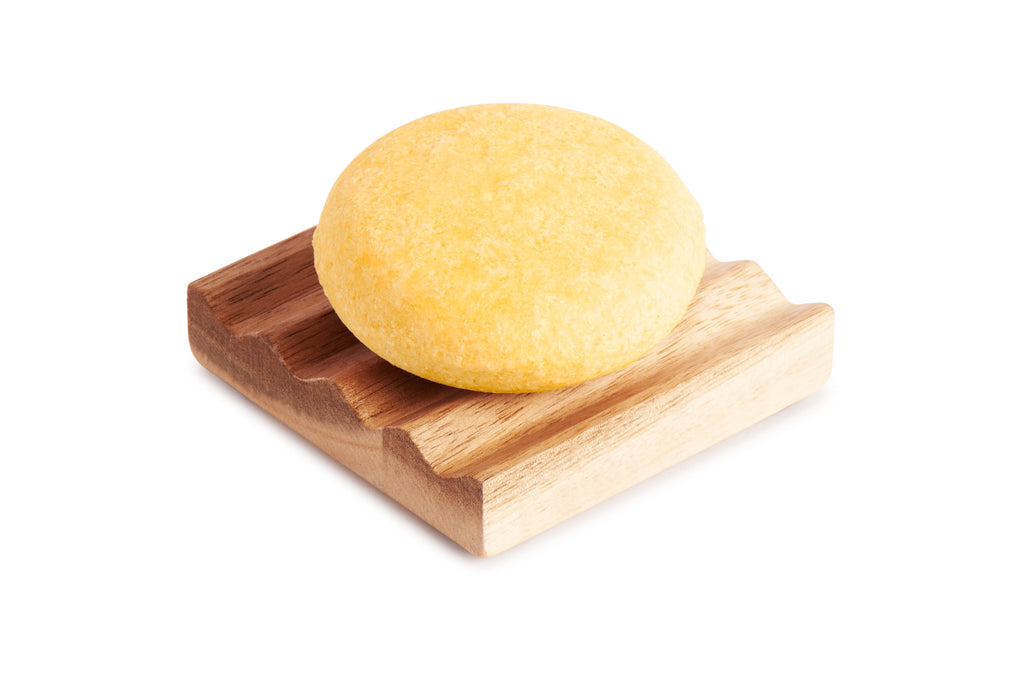 Yellow mango moisturizing shampoo bar on wooden soap holder, round and textured