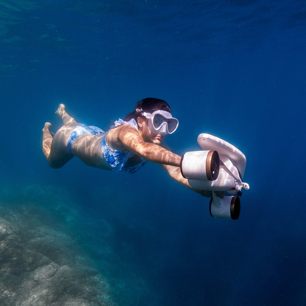Underwater camera device worn by diver, arms extended in blue water