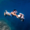 Underwater camera device worn by diver, arms extended in blue water