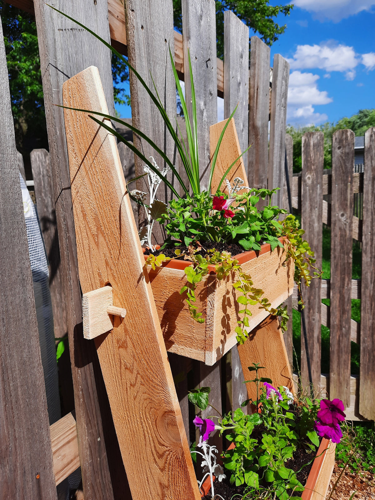 3-tier vertical cedar standing planter box with three wooden troughs holding potted plants