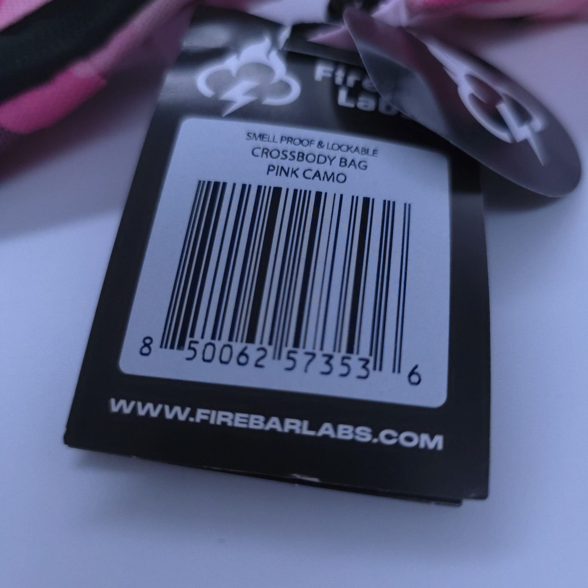 Pink camo crossbody bag with black tag showing barcode and website