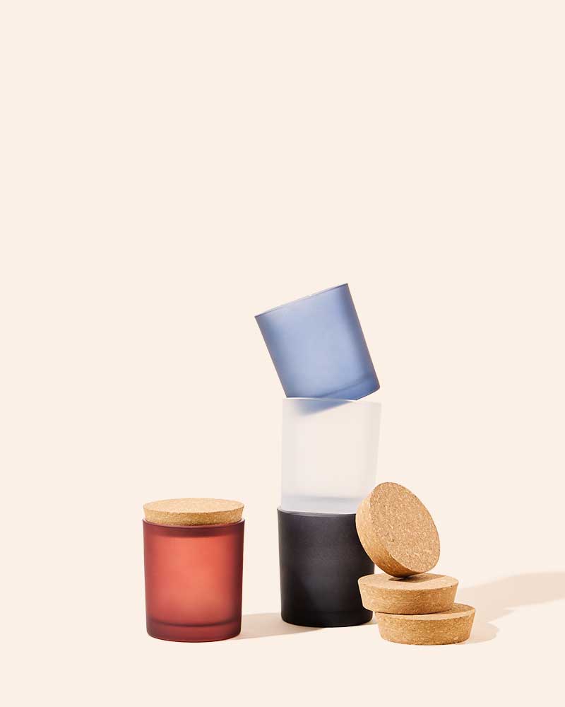 Set of frosted candle vessels with cork lids in amber, red, black, and blue