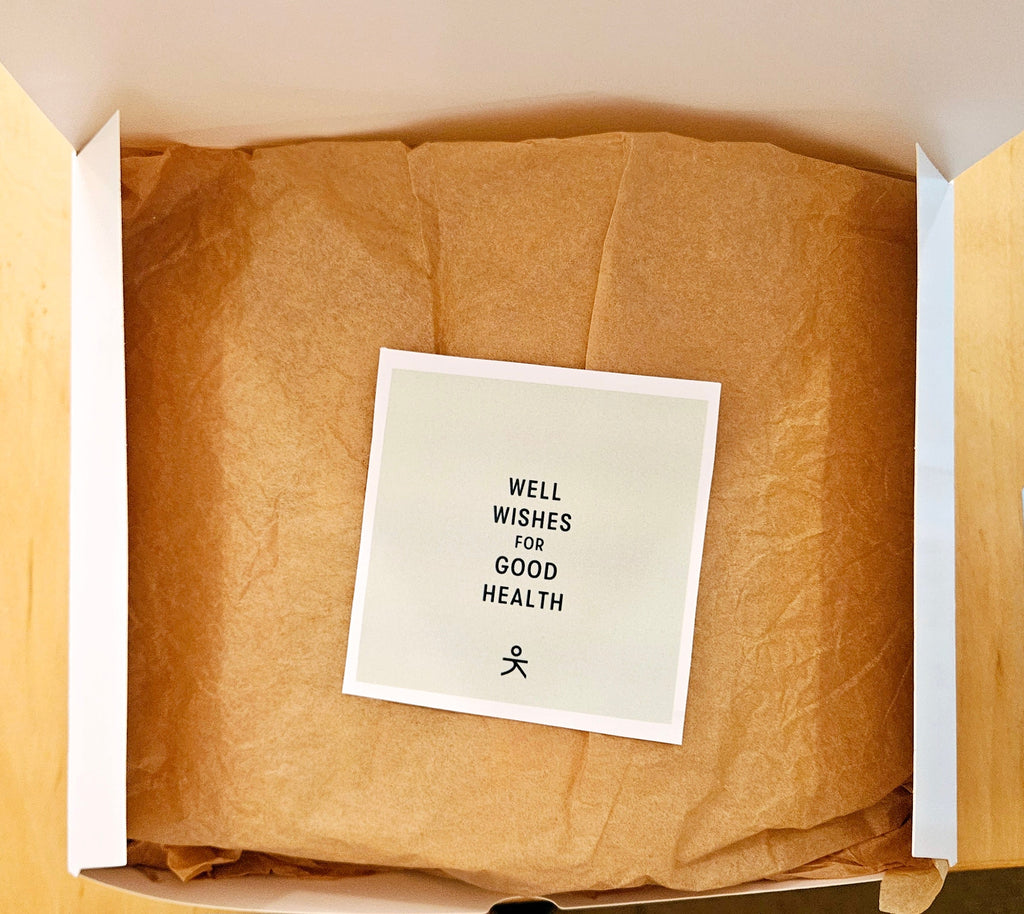 Open gift box with brown paper lining and a card reading “Well wishes for good health”