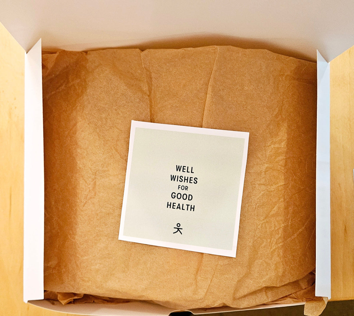 Open gift box with brown paper lining and a card reading “Well wishes for good health”