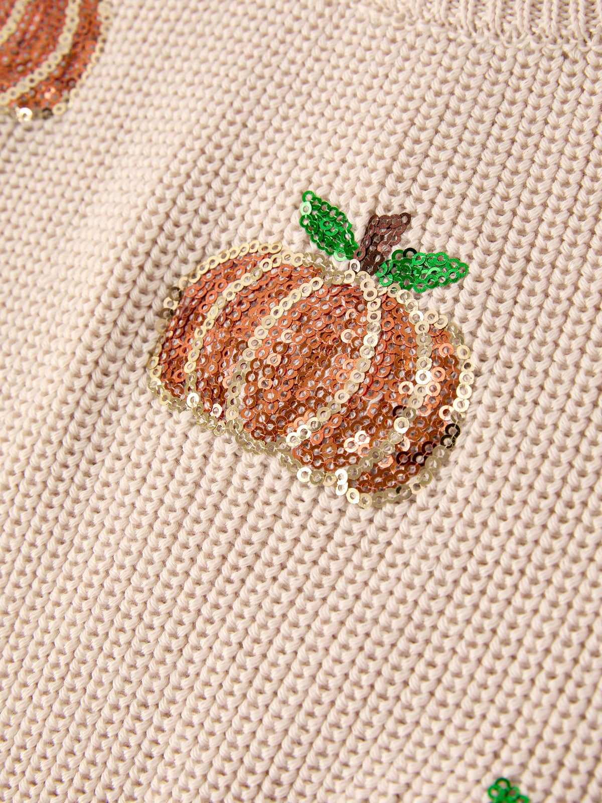 Close-up of sequined orange pumpkin with green leaf on beige knit sweater