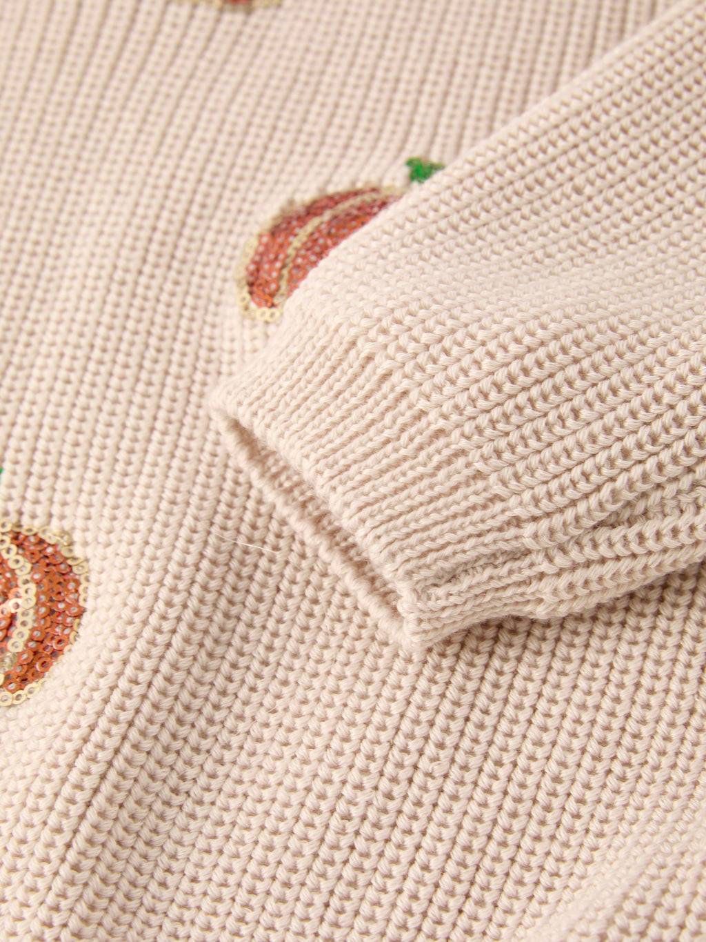 Beige knit sweater cuff with small sequined pumpkin motif