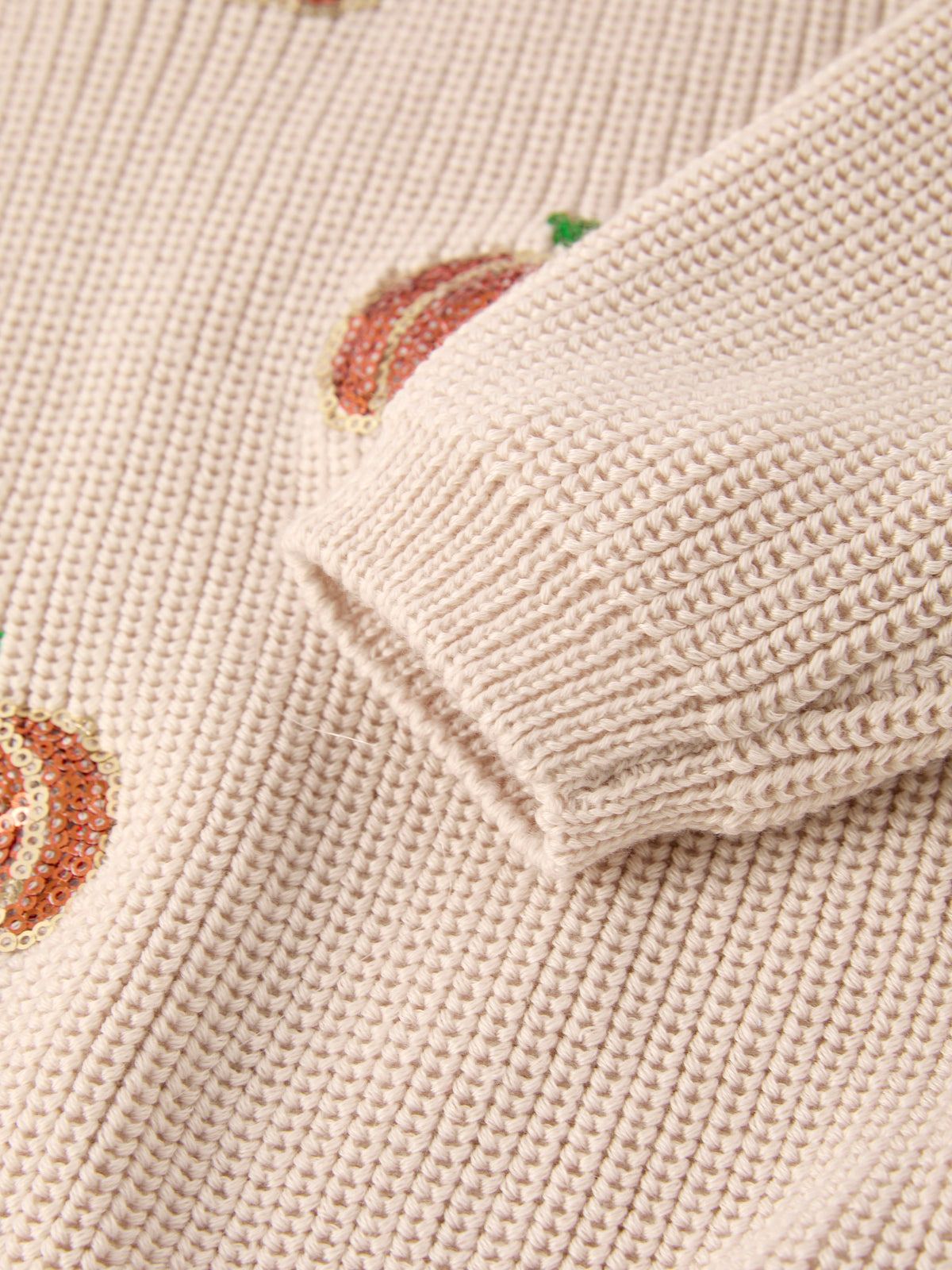 Beige knit sweater cuff with small sequined pumpkin motif