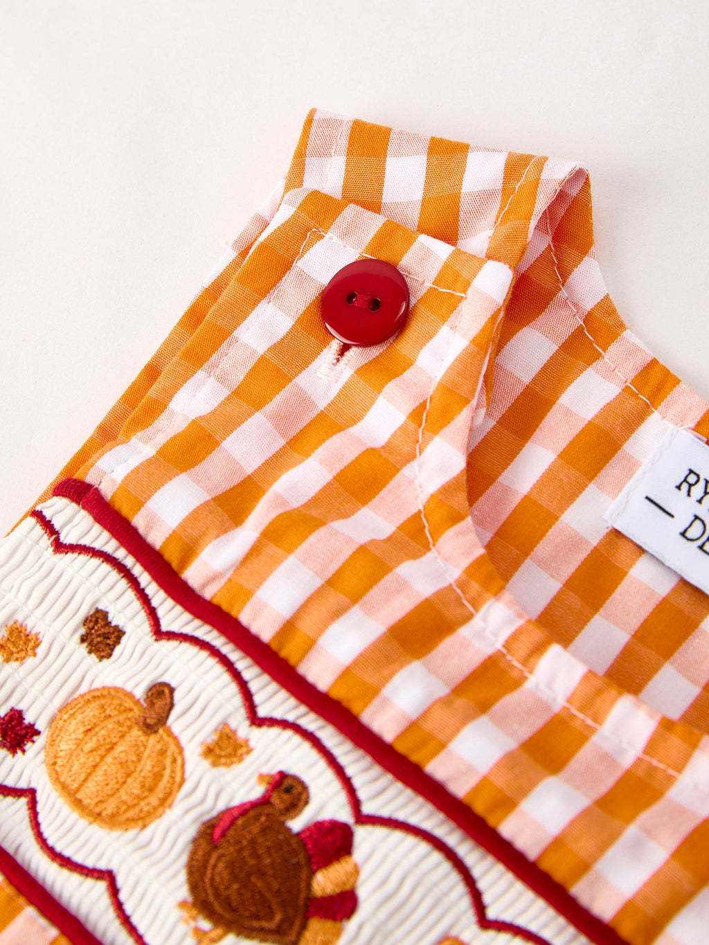 Orange-and-white gingham romper top with red button and embroidered turkey strip