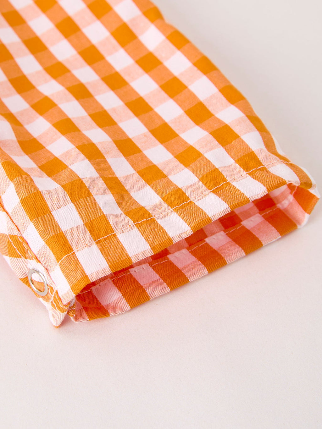 Orange-and-white gingham romper fabric close-up with stitched folded hem