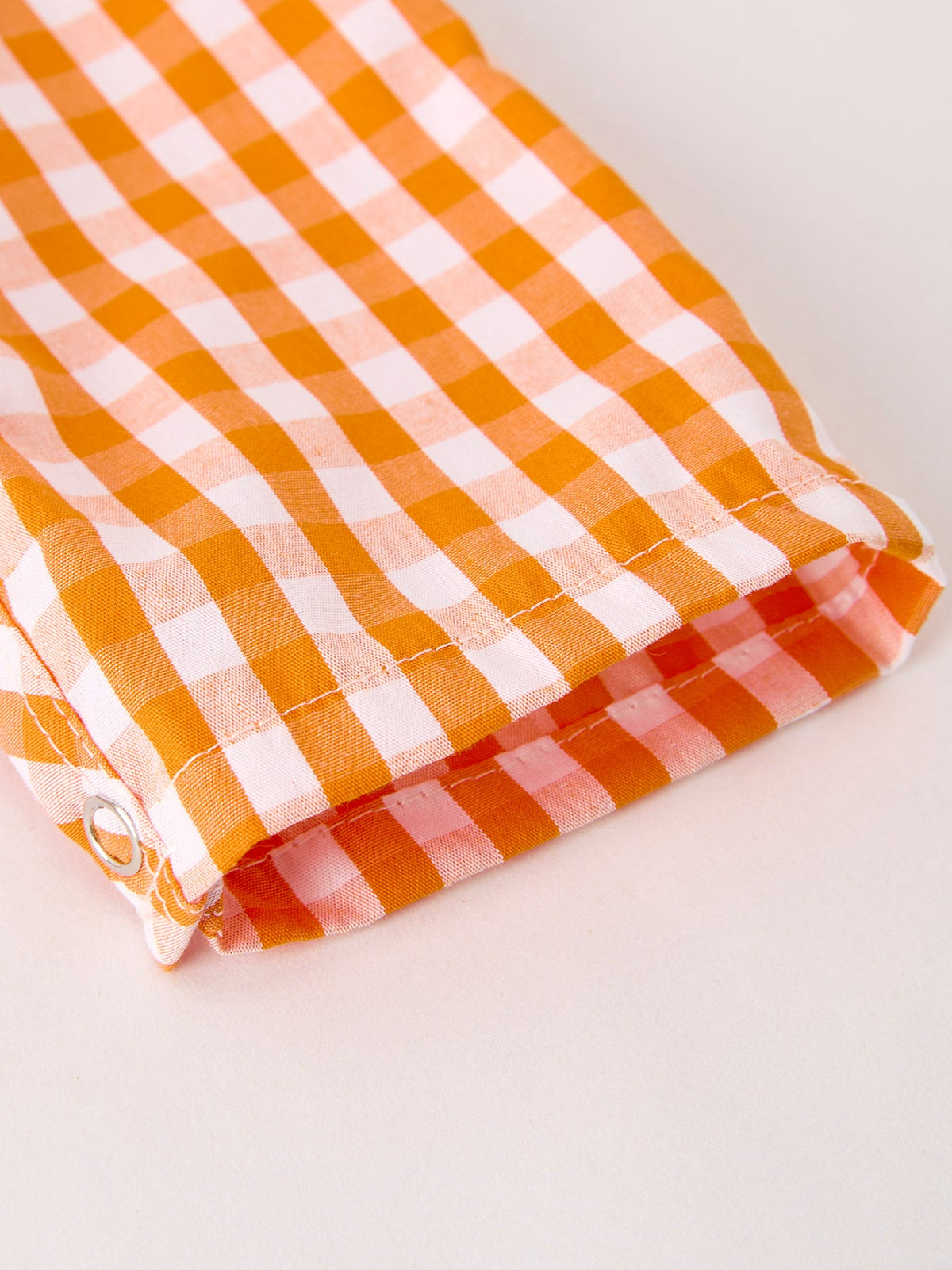 Orange-and-white gingham romper fabric close-up with stitched folded hem