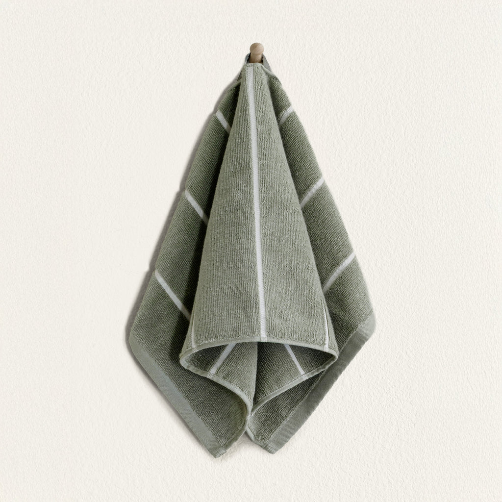 Sage green cotton towel with ecru border, folded and hanging