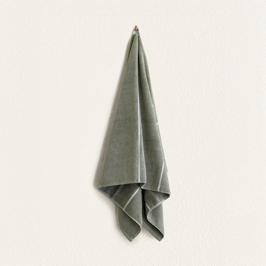 Sage green cotton towel folded with visible ecru trim along edges