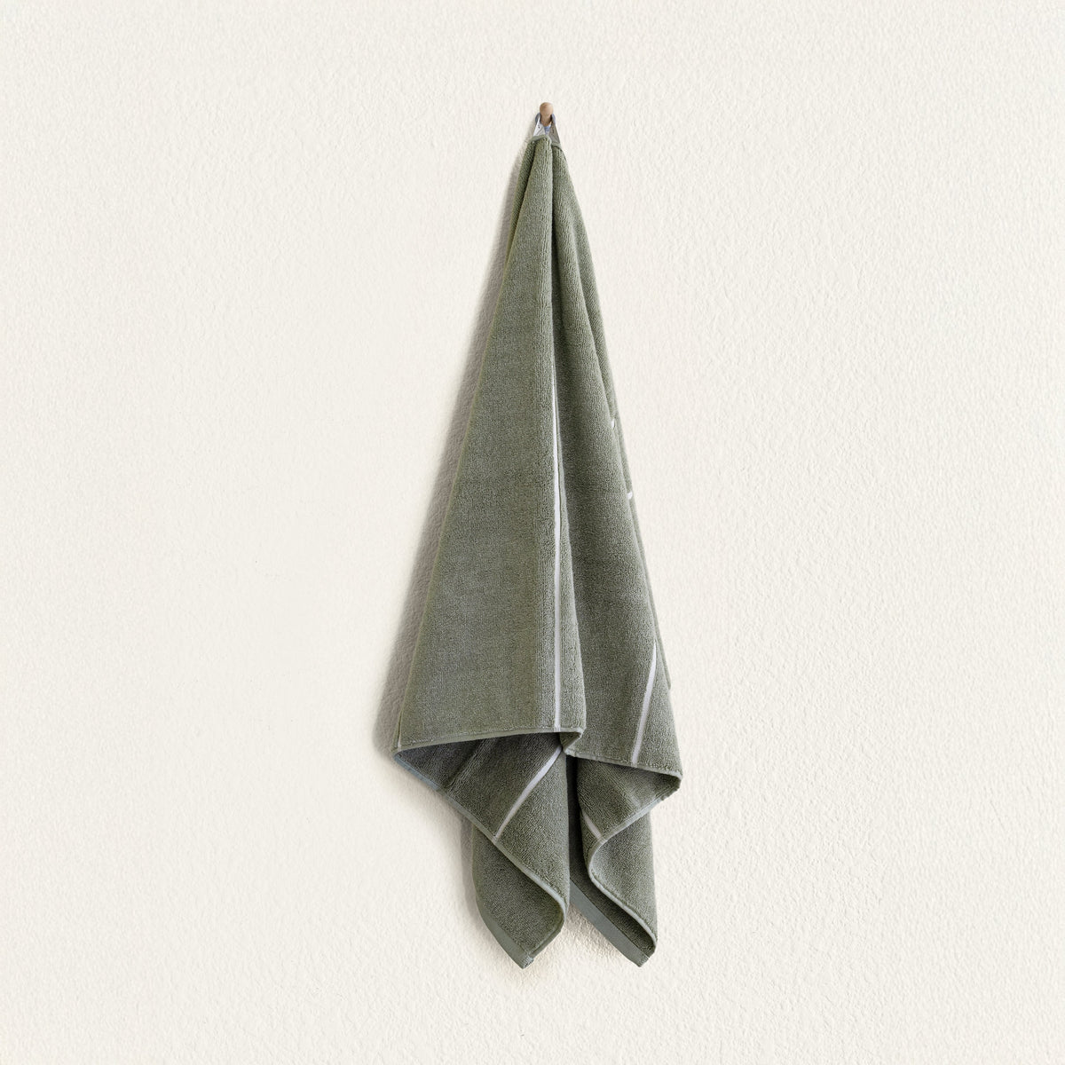 Sage green cotton towel folded with visible ecru trim along edges