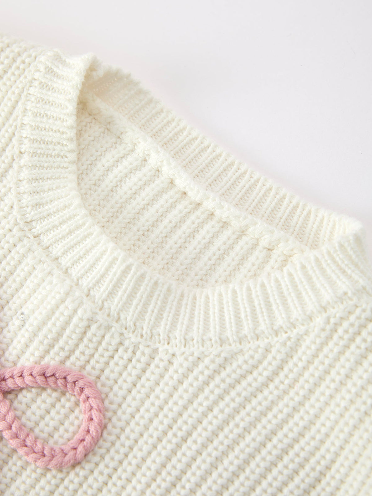 Cream knit crewneck sweater close-up with ribbed collar and pink bow tie