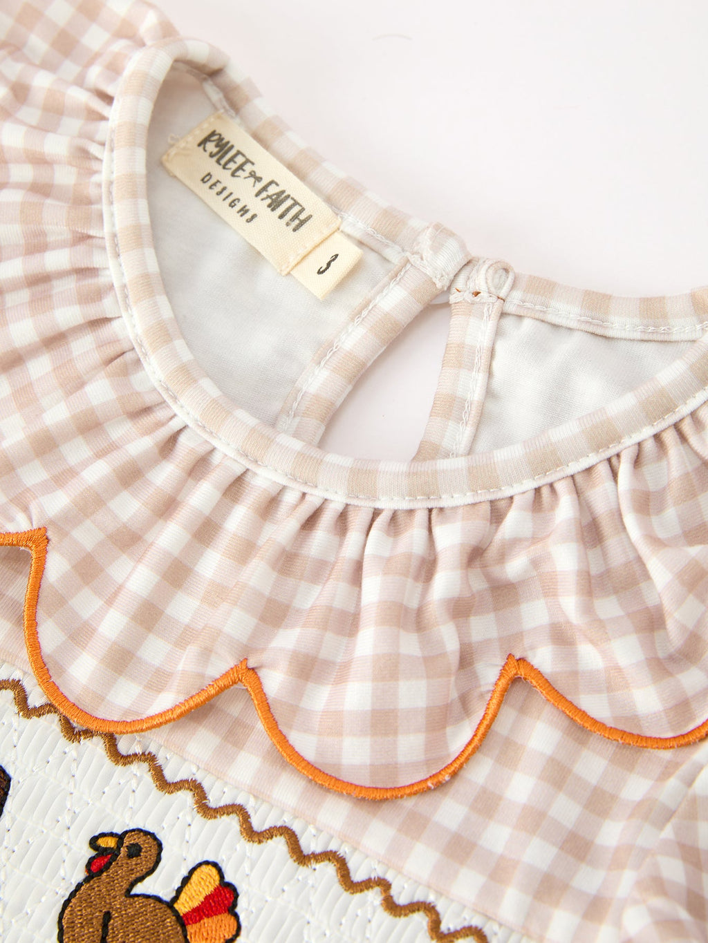Close-up of gingham dress neckline with orange scalloped trim and neck tag