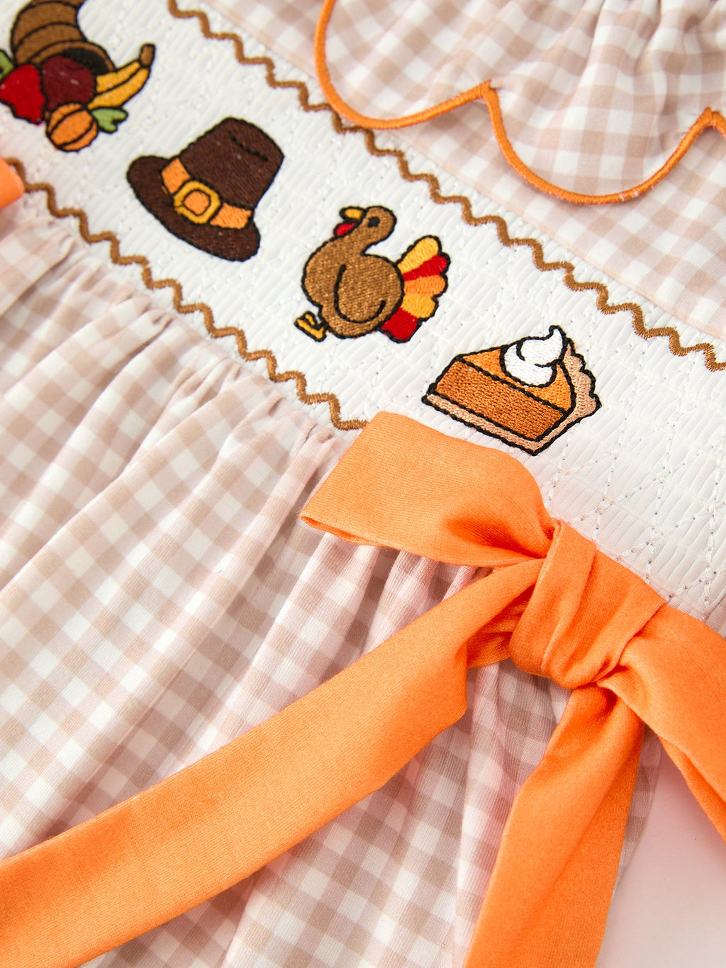 Close-up of Thanksgiving embroidery and orange bow on gingham dress bodice