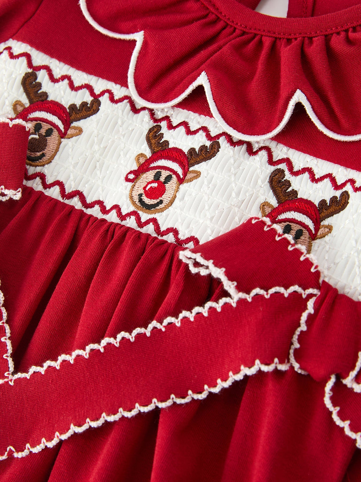 Close-up: red and white smocked bubble romper with embroidered reindeer faces and zigzag trim