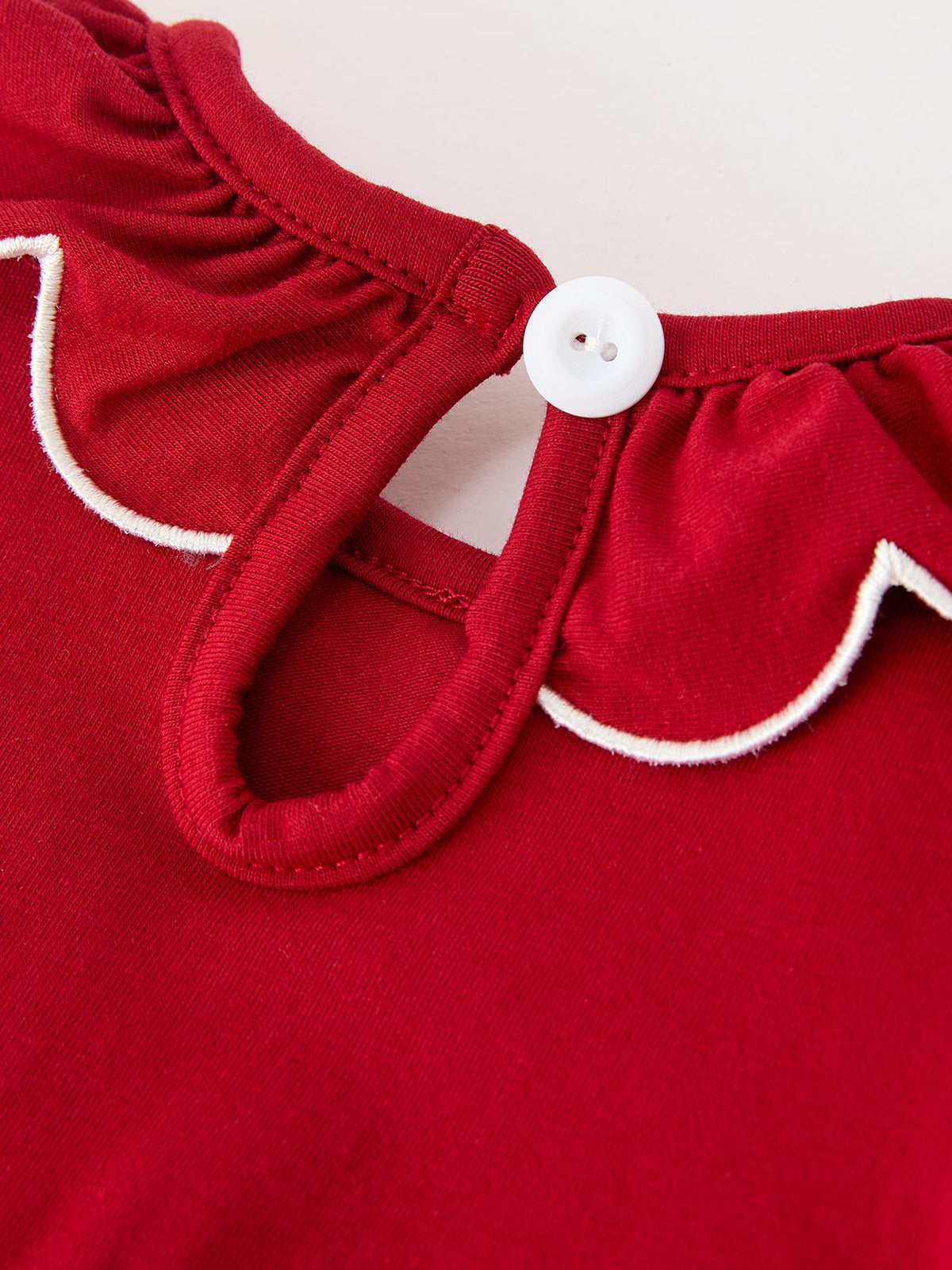 Red baby romper neckline with scalloped white trim and round white button closure