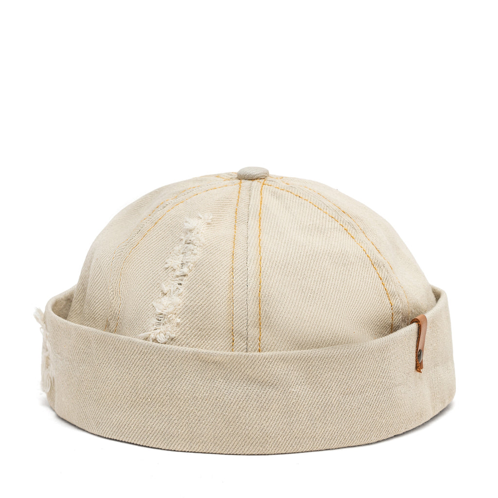 Beige canvas Docker-style cap top with vertical seams and small distressed embroidery