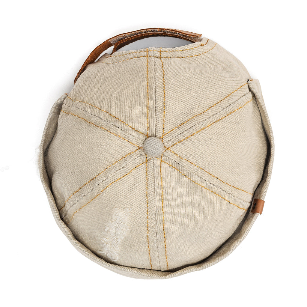 Beige canvas Docker-style cap with crown seams and brown leather strap detail