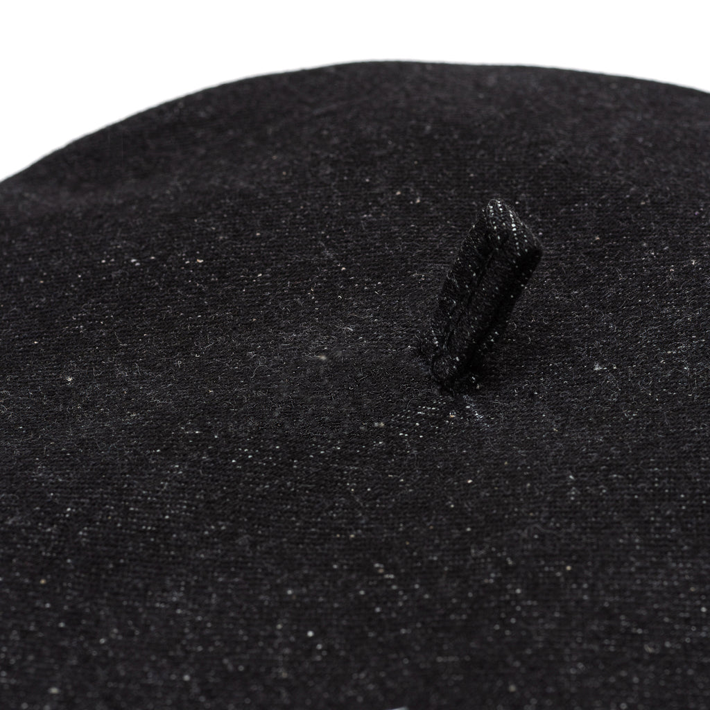 Black beret close-up showing textured fabric and small stitched top tab