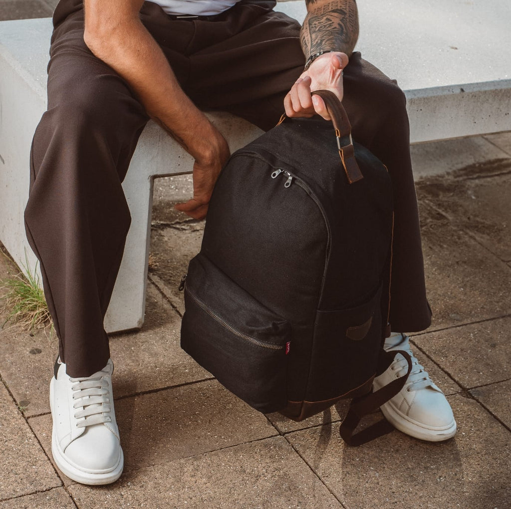 Dark canvas backpack with front zip pocket and leather-trimmed shoulder straps