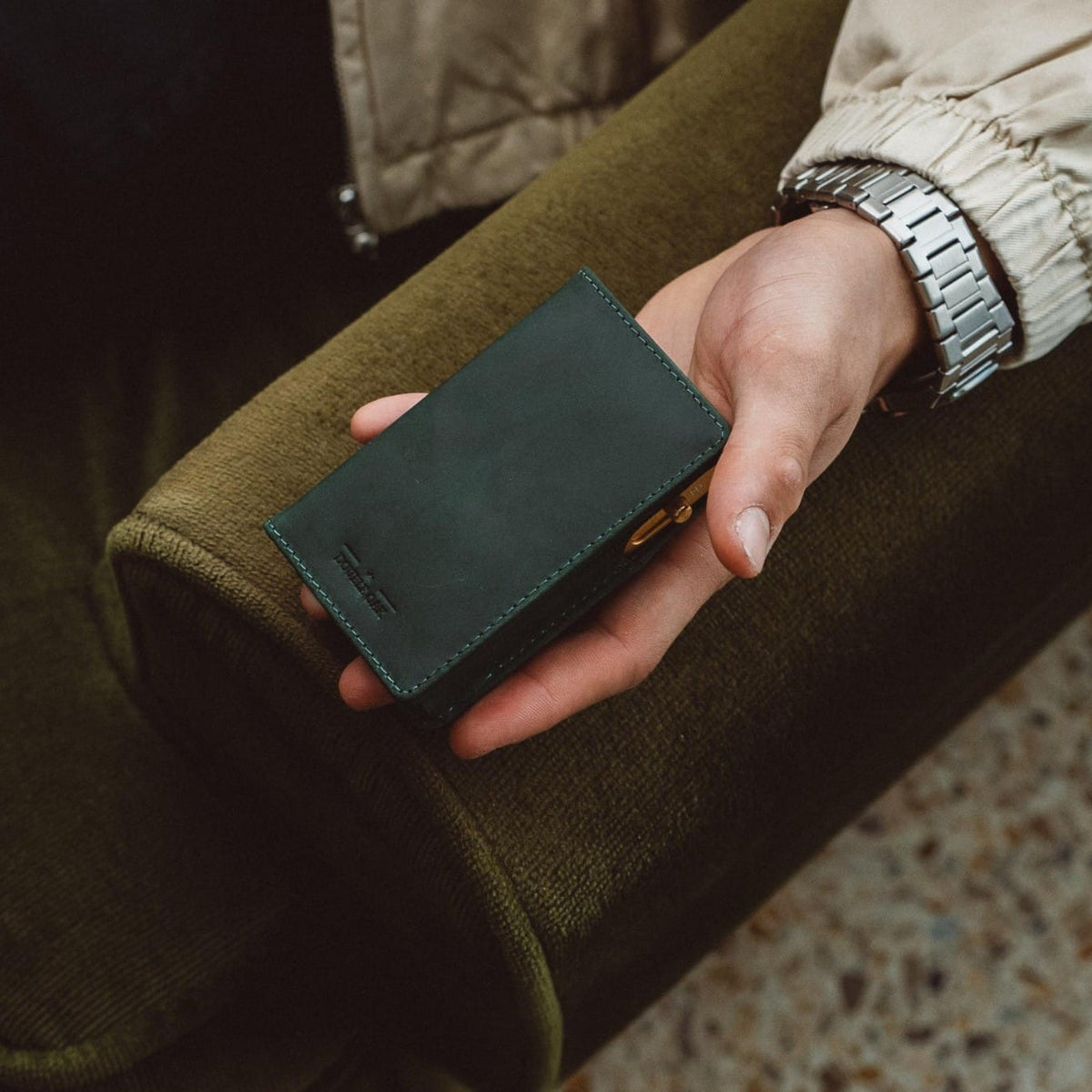 Bifold wallet in dark teal leather with stitched edges and folded front