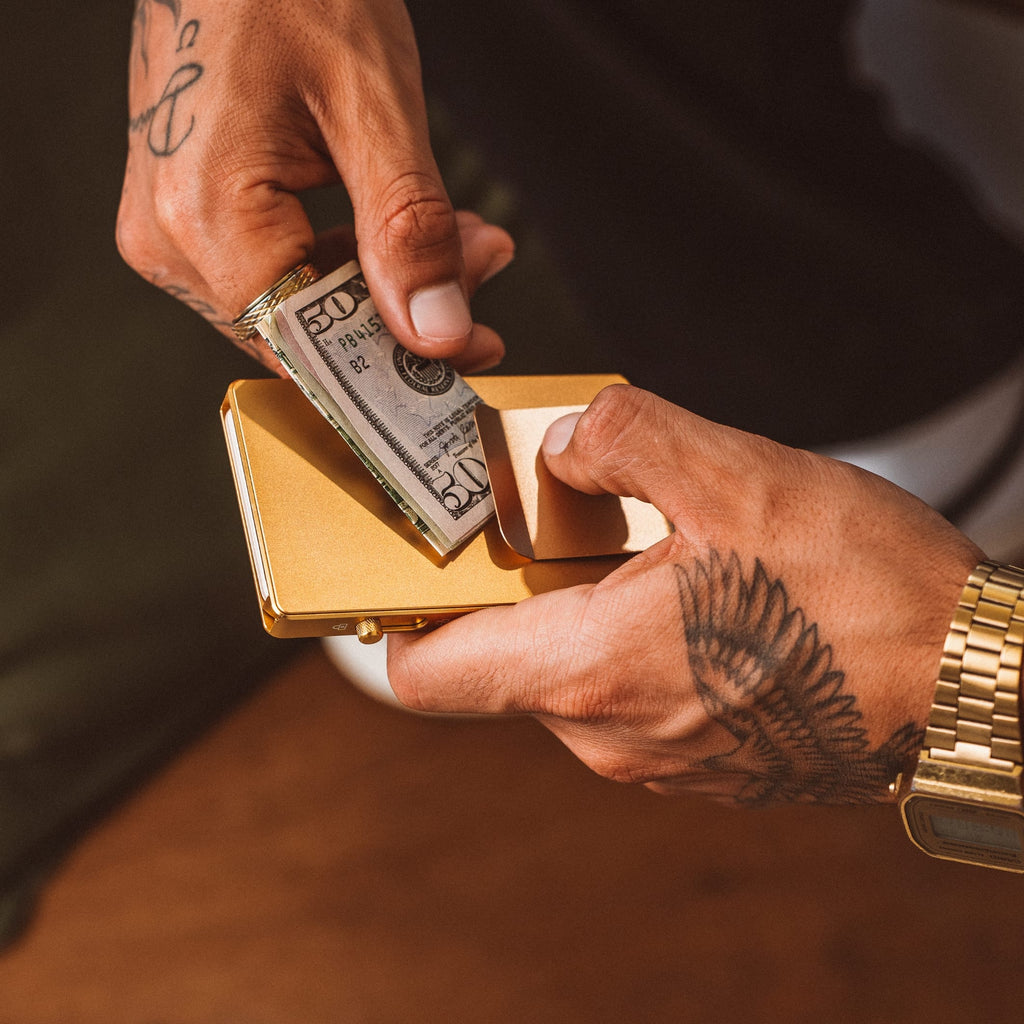 Open gold-tone mod wallet with tan interior holding cash and cards