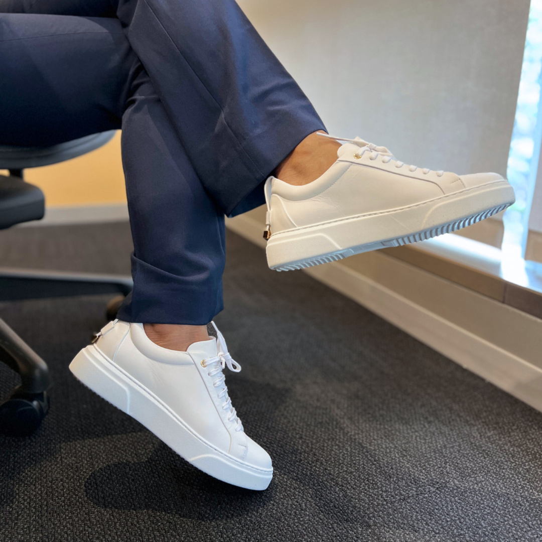 White low-top sneakers on feet with light blue-striped outsole trim