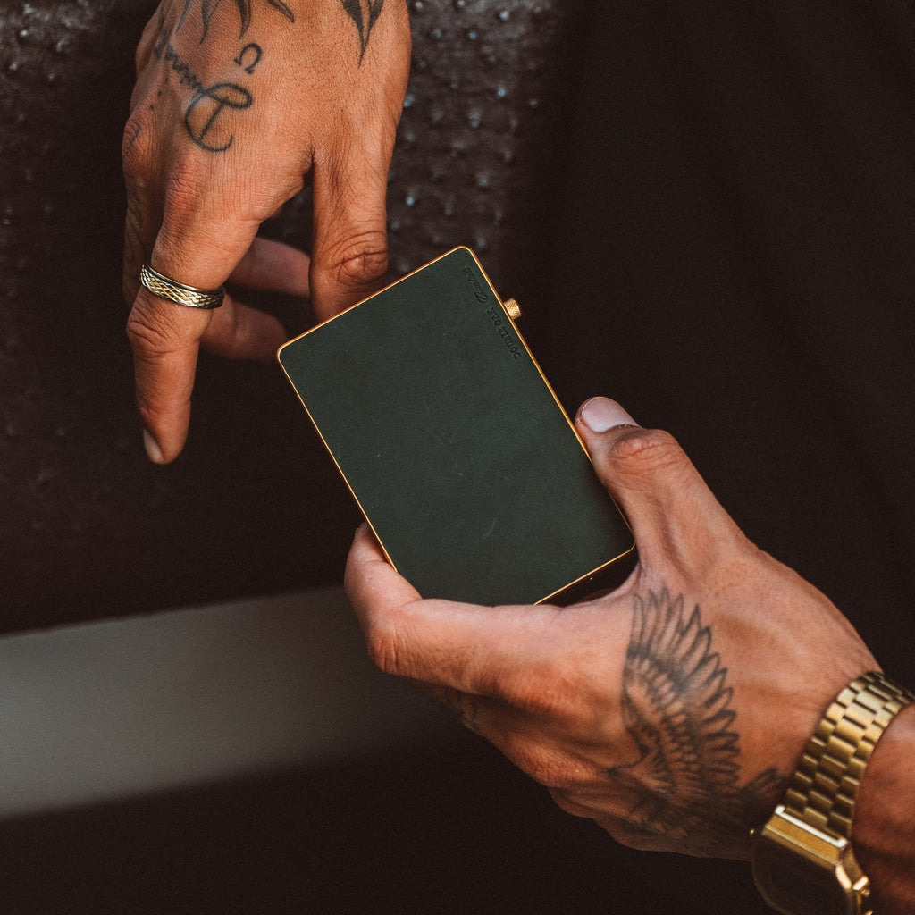 Mod wallet cardholder closed in dark finish with gold-tone edges, hands gripping the corners