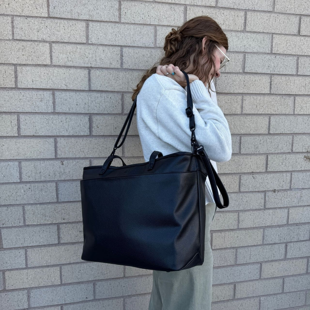 Dark tote bag with crossbody strap and top handle, carried over shoulder