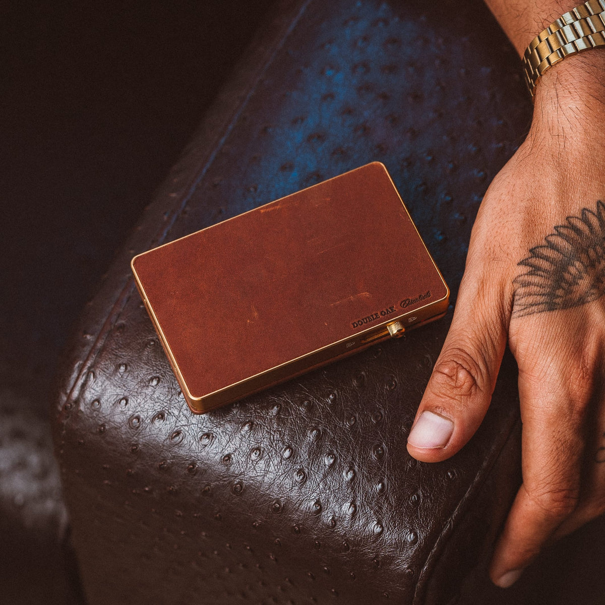 Brown leather mod wallet with gold trim and a metal clasp, resting on a leather surface