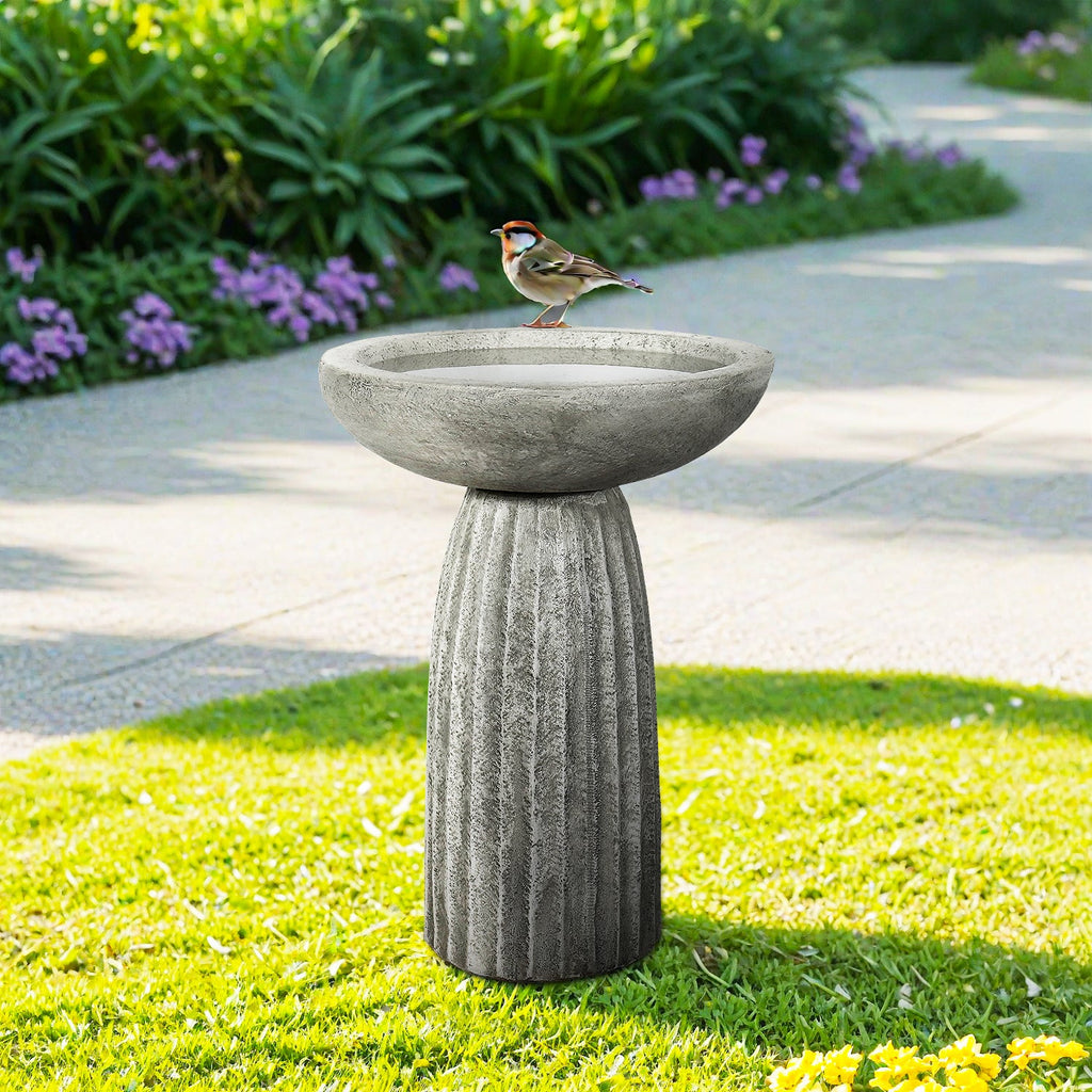 Concrete bird bath with round bowl and fluted pedestal on outdoor lawn