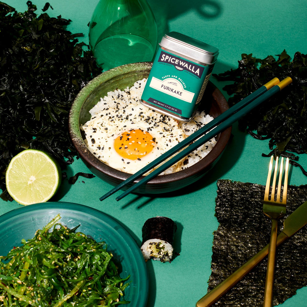 Green Furikake seasoning tin with silver lid, surrounded by sesame spice flakes