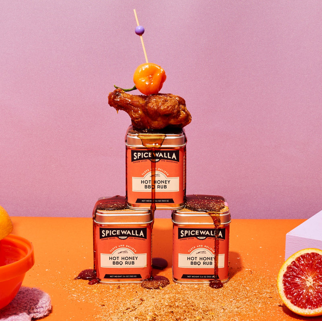 Stack of Spicewalla Hot Honey BBQ Rub seasoning tins with a small heap of rub.