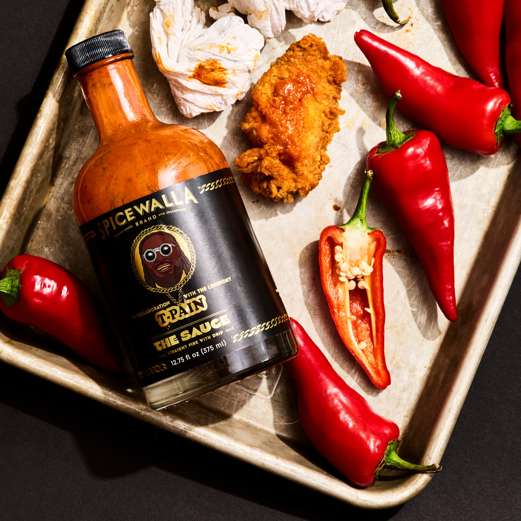 Spicewalla sauce bottle with orange glass, shown with peppers on a serving tray.